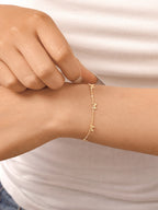 18K gold Bellina bow charm bracelet worn on the wrist, featuring delicate bow-shaped charms on a fine chain in a close-up lifestyle image.