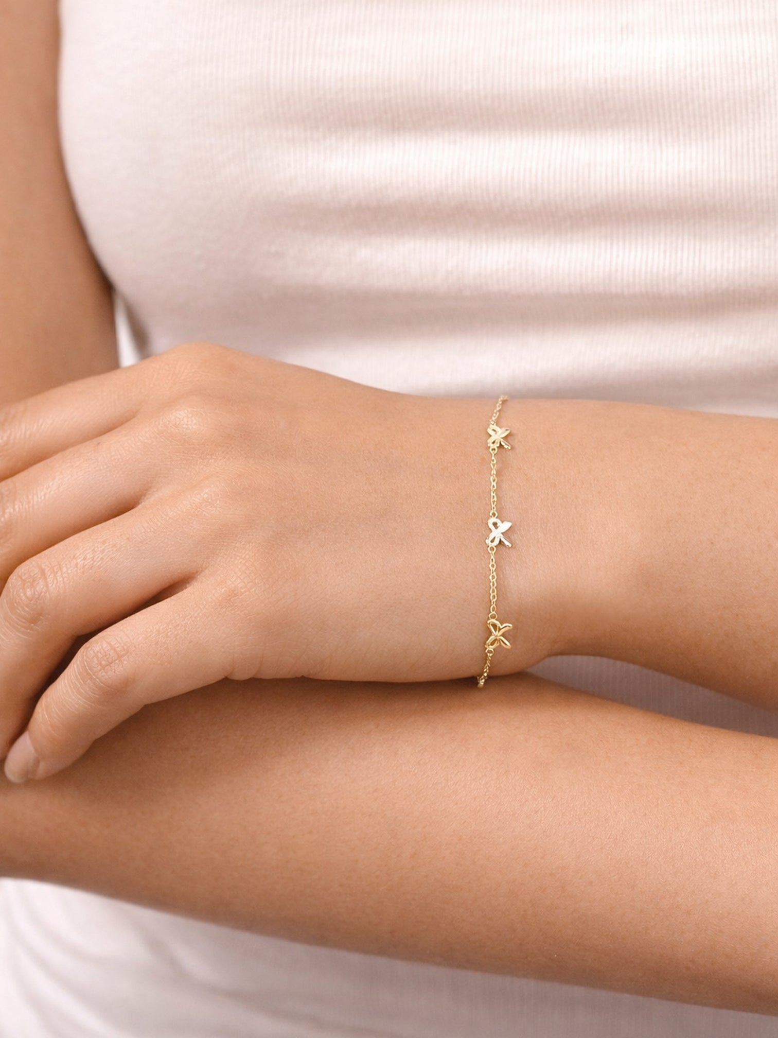 18K gold Bellina bow charm bracelet styled on the wrist, showcasing multiple small bow charms along a dainty chain in a minimal lifestyle shot.