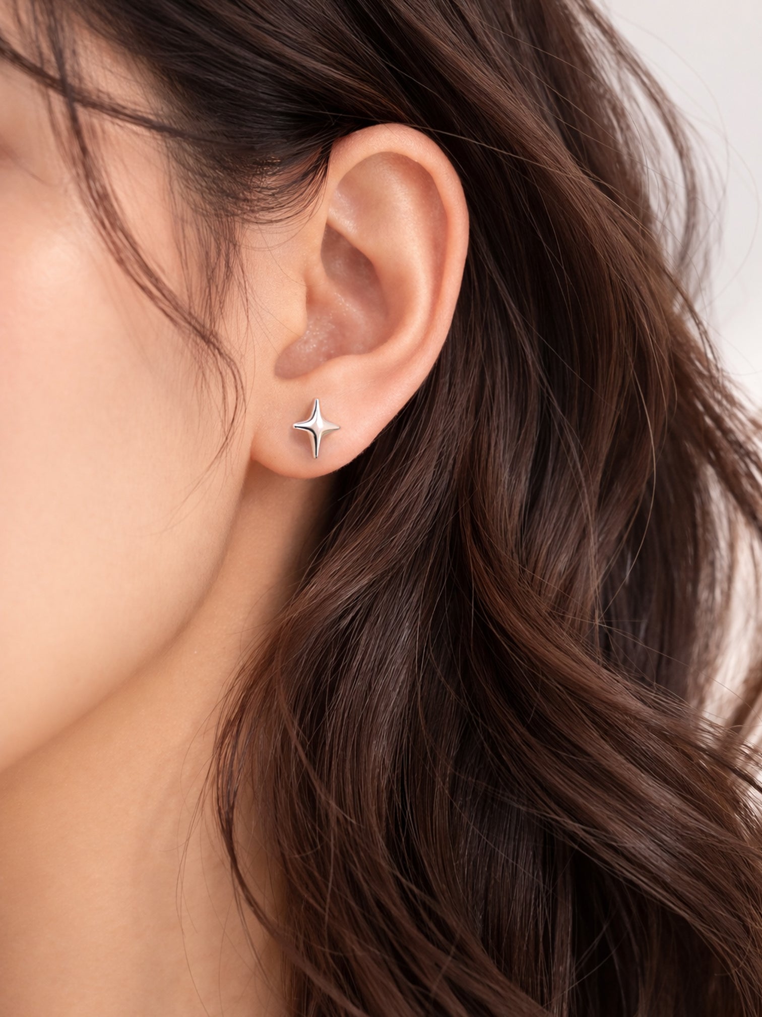white gold Starry screwback star stud earrings worn on the ear in a close-up lifestyle image, featuring a sleek four-point star silhouette.