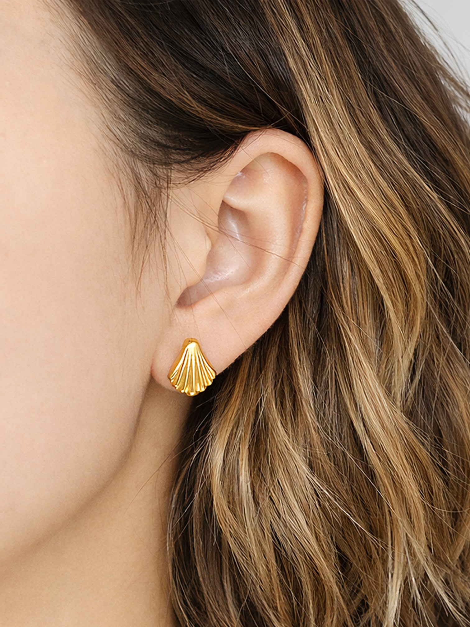 Solana screwback earrings in 18K gold plated finish, featuring a delicate shell-inspired fan design, worn on the ear in a close-up lifestyle shot.