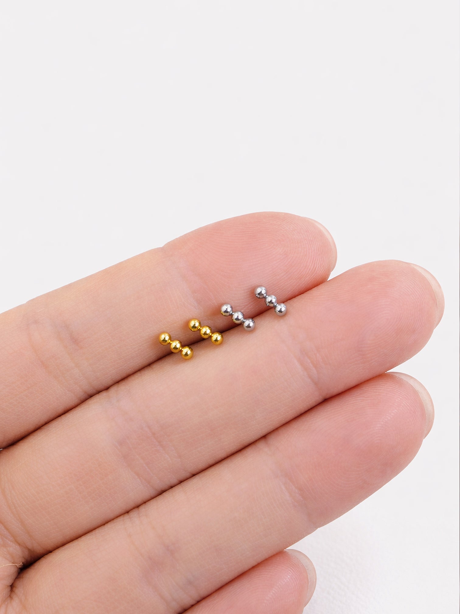 Zane gold and white gold triple ball stud earrings size comparison on fingertip | myEdzy