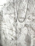 Silver adjustable Y lariat necklace with dual chain layers, featuring a sleek snake chain drop and polished oval link chain, set against textured white stone background.