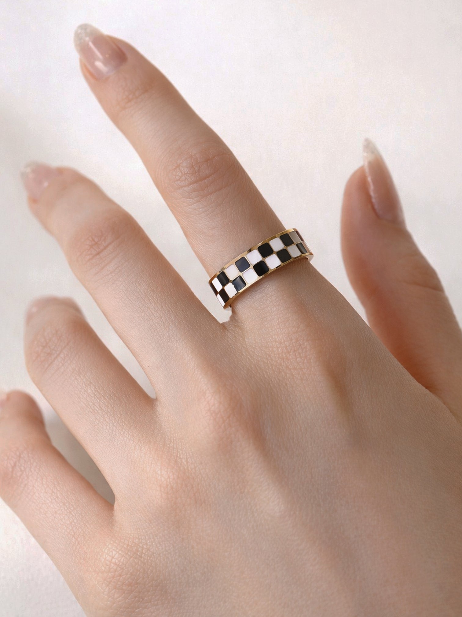 Irelina black and white checkered enamel statement band ring in 18K gold plating worn on finger, minimal clean background close-up by myEdzy