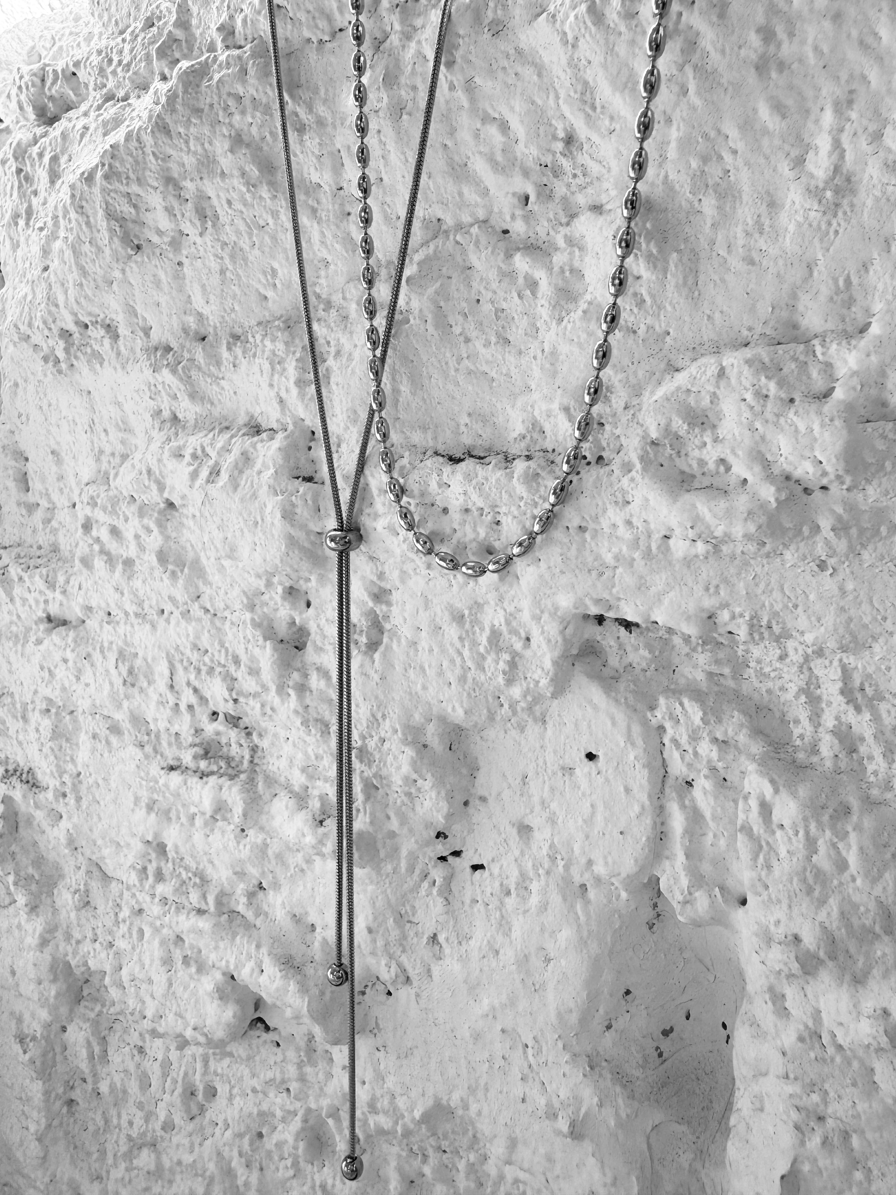Minimal silver necklaces styled on a textured wall, showcasing modern everyday jewelry designed in Las Vegas with a clean, contemporary aesthetic